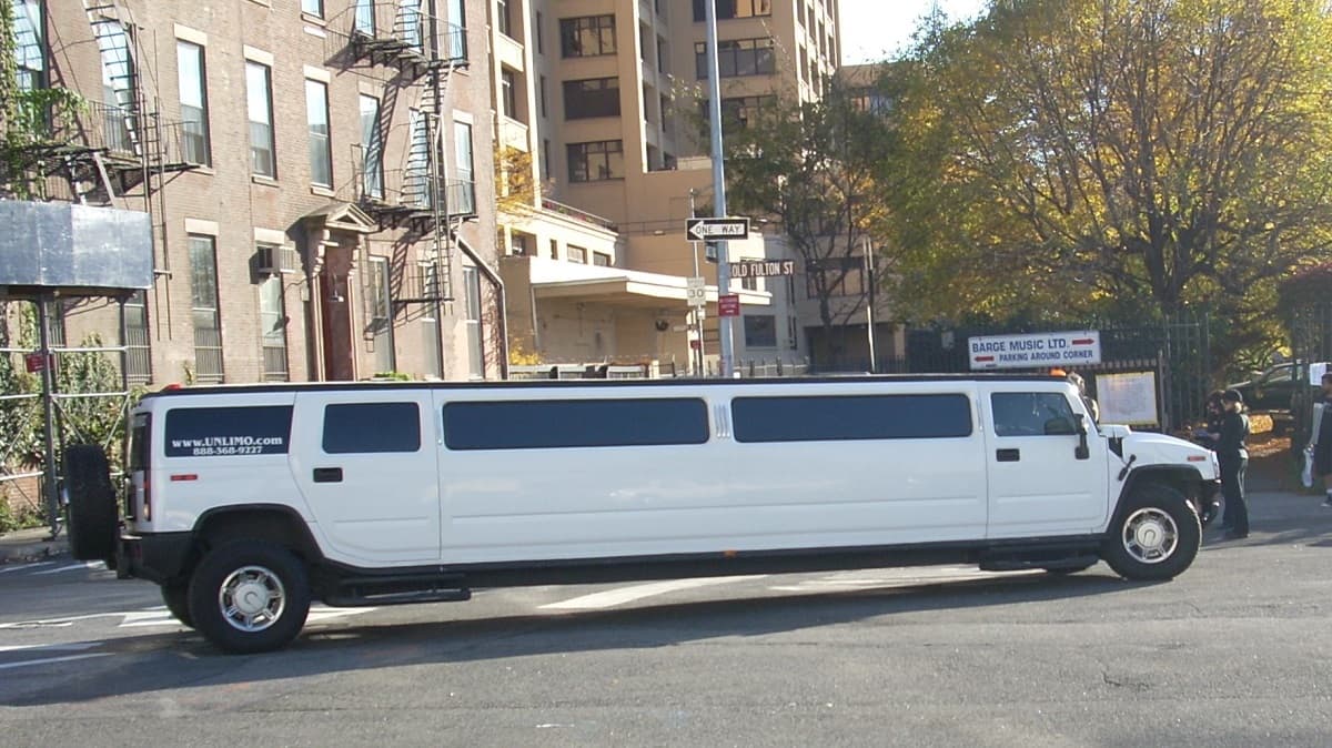 ニューヨーク、ブルックリンのオールド・フルトン・ストリートに駐車されている白いハマーH2のストレッチリムジン。周囲には古い建物や「BARGE MUSIC LTD」の看板、街路樹が見える。