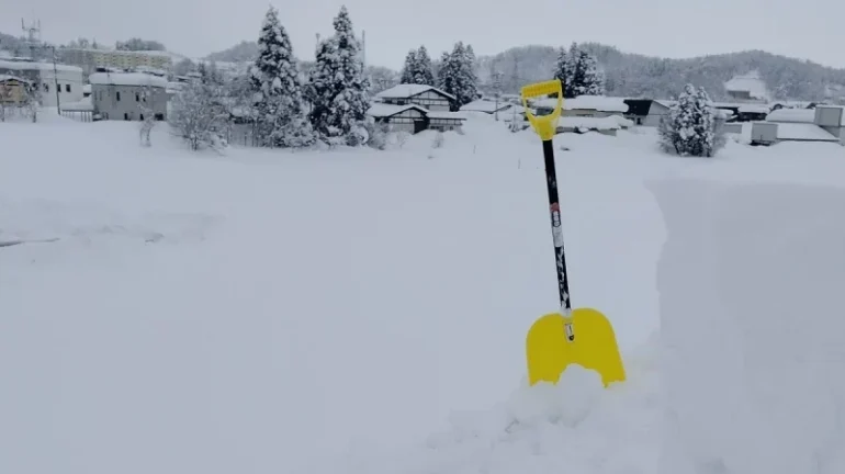 屋根の上から見た、深く積もった雪と黄色い雪かきスコップ