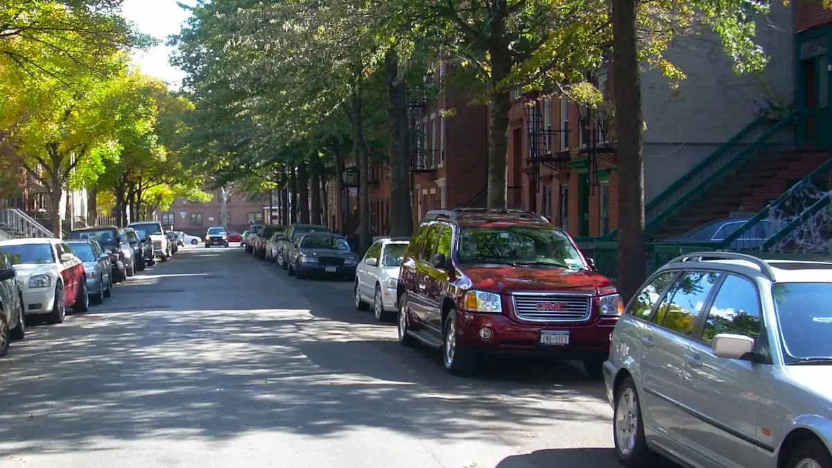 ニューヨーク、ブルックリンの通りに縦列駐車された複数の車と街路樹、奥に見える古いレンガ造りのアパートメント。