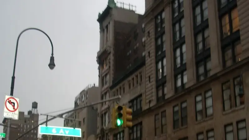 ニューヨーク市マンハッタンの6番街の交差点。左折禁止（）、一方通行を示す道路標識、「6 AV」の緑色の道路標識が確認できる。背景には古い石造りの建物（）や近代的な高層ビルが混在している。 