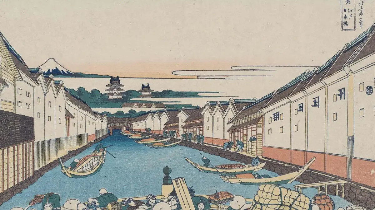 葛飾北斎による浮世絵。画面下部に日本橋を渡る人々の頭部が見え、中央を貫く運河には多くの舟が浮かび、両岸には蔵が立ち並ぶ。運河の先には江戸城の石垣と櫓、そして遠くに富士山が描かれた『冨嶽三十六景 江戸日本橋』の図。