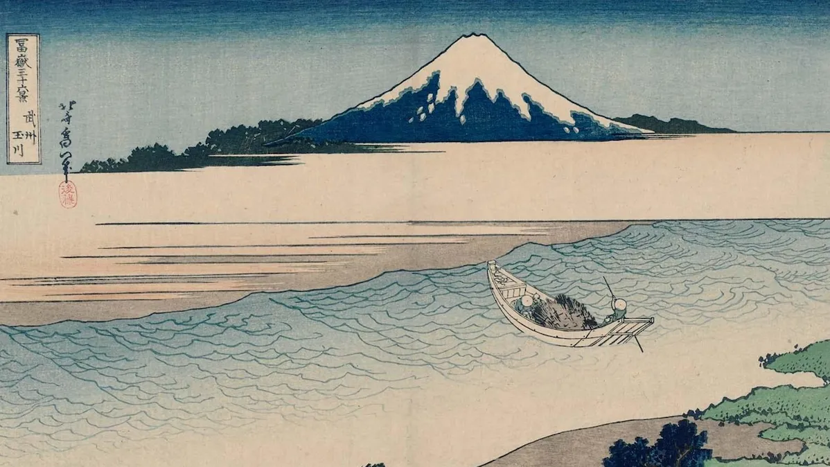 葛飾北斎による浮世絵。手前に多摩川の流れと荷を積んだ舟や馬が描かれ、遠景には雪を頂いた富士山がそびえる。落ち着いた青と茶の色彩が特徴的な『冨嶽三十六景 武州玉川』の図。